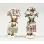 TWO SMALL MEISSEN PORCELAIN FIGURES OF YOUNG GIRLS holding a bundle above their head , with