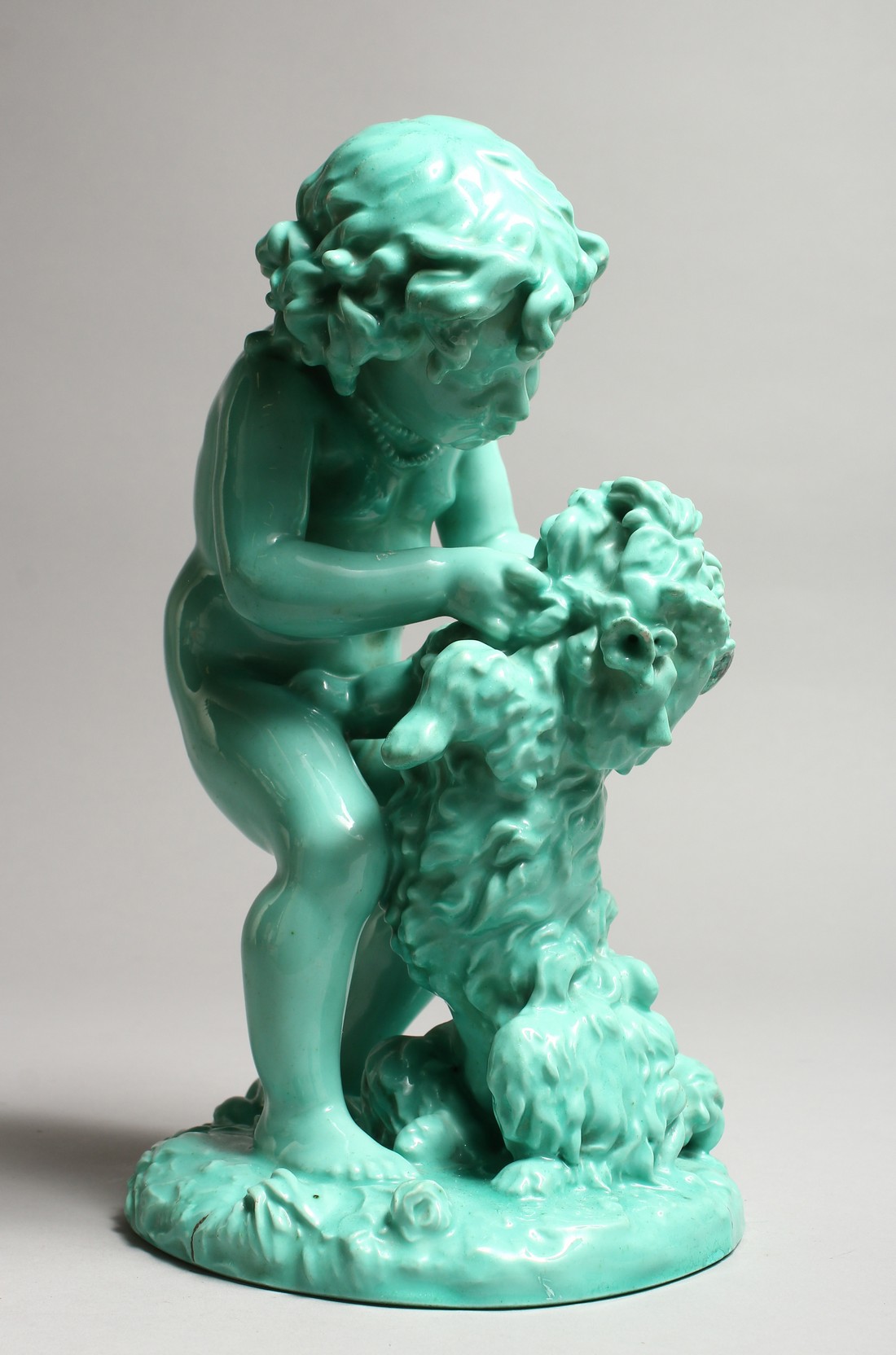 A CONTINENTAL TURQUOISE GLAZED POTTERY FIGURE of a young girl playing with a dog. 11ins high.