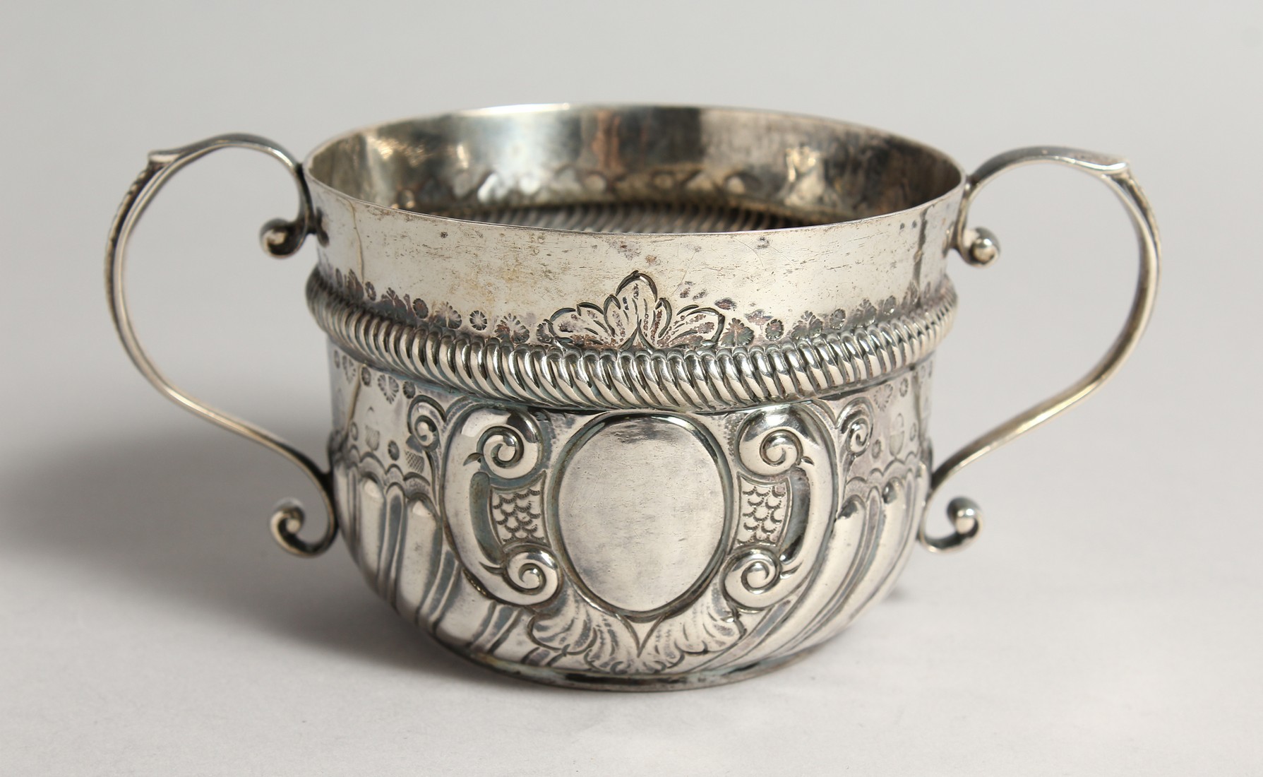 A QUEEN ANNE TWO HANDLED CIRCULAR PORRINGER, wrythen fluted handles, London 1709, maker J. JACKSON