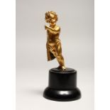 A GOOD SMALL GILDED METAL MODEL OF A CHERUB, standing with a cloak draped over one shoulder, on a