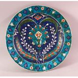 A TURKISH OTTOMAN IZNIC STYLE POTTERY PLATE, with a blue ground and floral decoration 30cm.