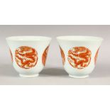 A PAIR OF RED AND WHITE CUPS, each with four panels of dragons and phoenix, 9.5cm high.