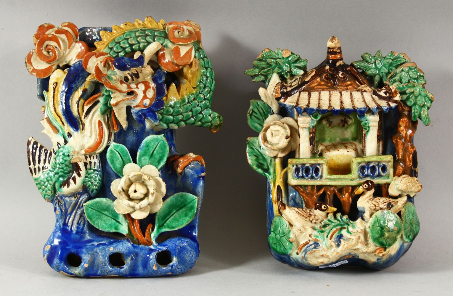 TWO CHINESE POLYCHROME POTTERY WALL POCKETS, carved with a shrine and flora with ducks / birds, 20cm