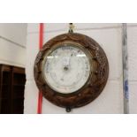 A circular aneroid barometer with carved oak frame.