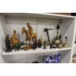 A shelf of decorative ornamental items to include brass bells, carved wood figures etc.