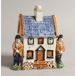 A 19TH CENTURY PRATTWARE MODEL OF A COTTAGE, with a male figure standing to each side. 4ins wide x