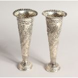 A PAIR OF VICTORIAN SILVER TAPERING VASES with repousse decoration and circular loaded bases. London