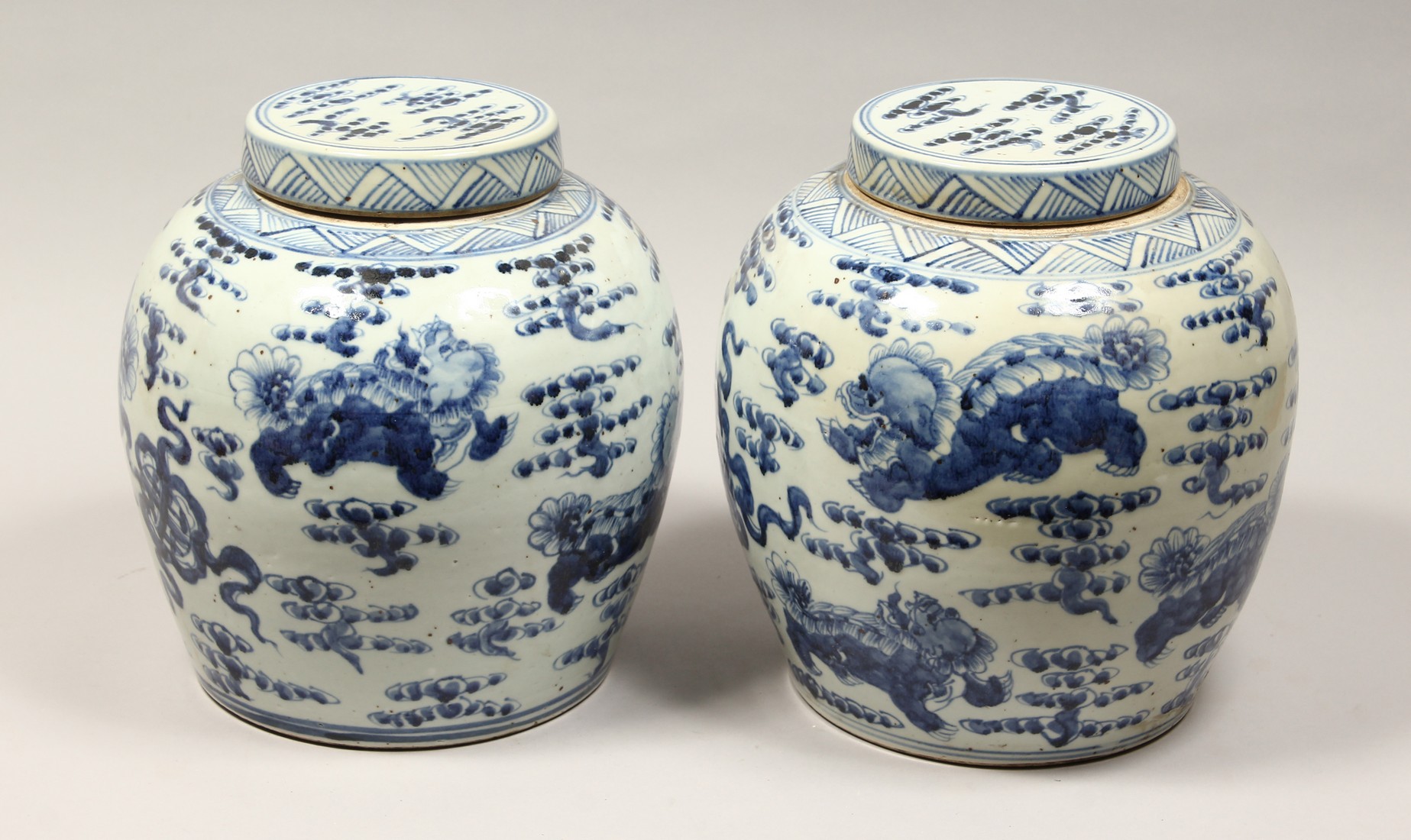 A PAIR OF CHINESE BLUE AND WHITE PORCELAIN JARS AND COVERS, painted with lion dogs 12.5ins high.