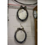 A pair of continental porcelain encrusted oval mirrors with cherub crestings.