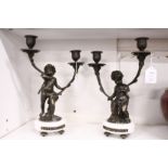 A pair of ornate twin branch candelabra modelled as cherubs holding two branches, on a marble base.