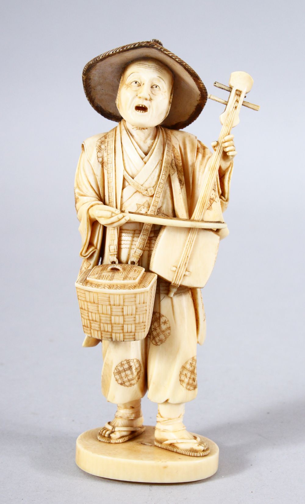 A JAPANESE MEIJI PEPRIOD CARVED IVORY OKIMONO - MUSICIAN - the figure stood holding his basket and