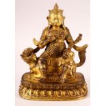 A CHINESE GILT BRONZE MODEL OF A DEITY, possibly Jambhala, seated upon a mythical creature, 22.5cm