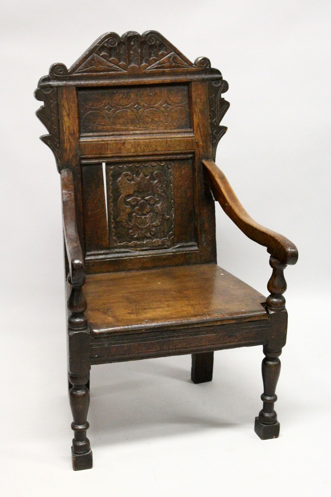 AN 18TH CENTURY OAK ARMCHAIR, with carved cresting rail and panelled back, solid seat and curving