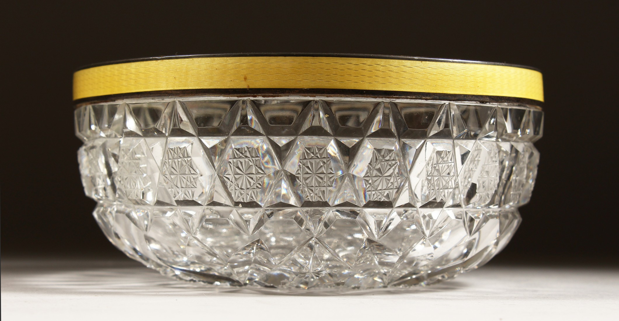 A CUT GLASS CIRCULAR BOWL with silver and yellow enamel rim 6ins diameter.