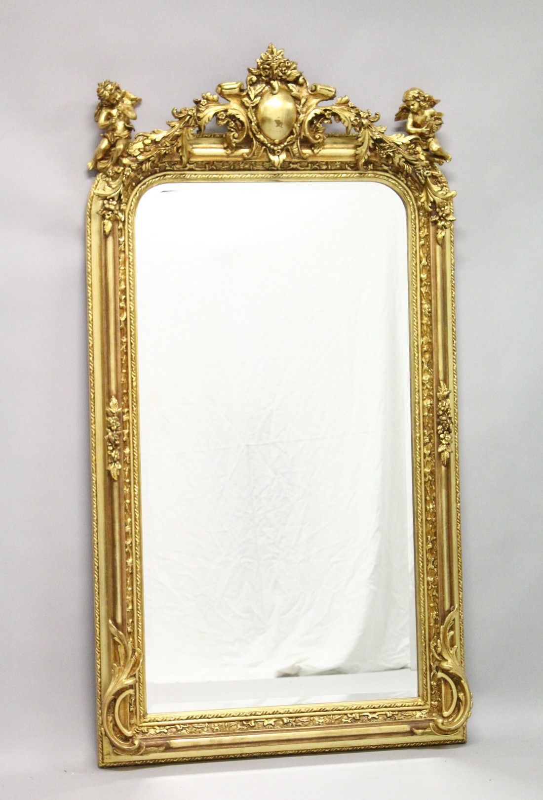A LARGE DECORATIVE GILT FRAMED MIRROR, the shaped top mounted with cherubs. 5ft 3ins high x 2ft 9ins