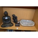 Two figures of Buddha, a stone trough and a cigarette box.