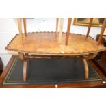 A burrwood oval shaped coffee table with galleried top on X-shaped supports.