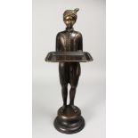 A CAST BRONZE FIGURE OF A STANDING MALE, his arms outstretched, holding a tray, on a circular