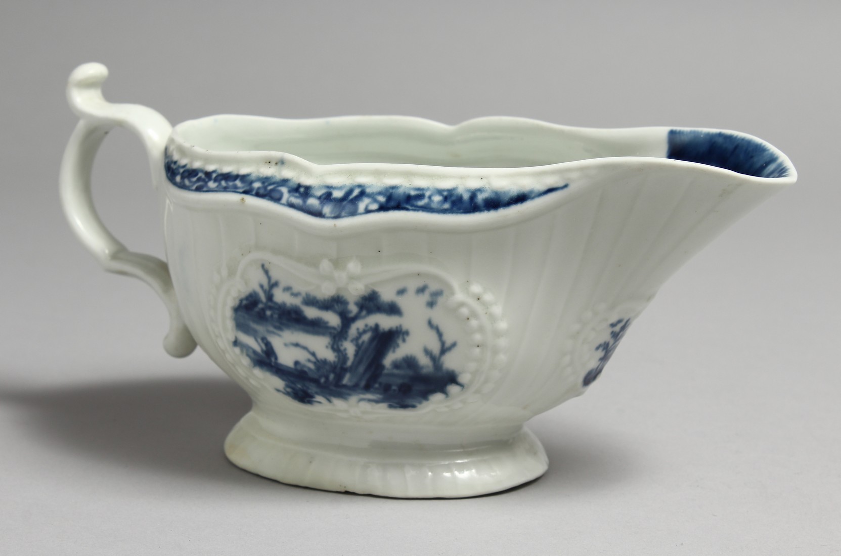 AN 18TH CENTURY WORCESTER SAUCEBOAT, with strap moulded body painted with Chinoiserie landscapes