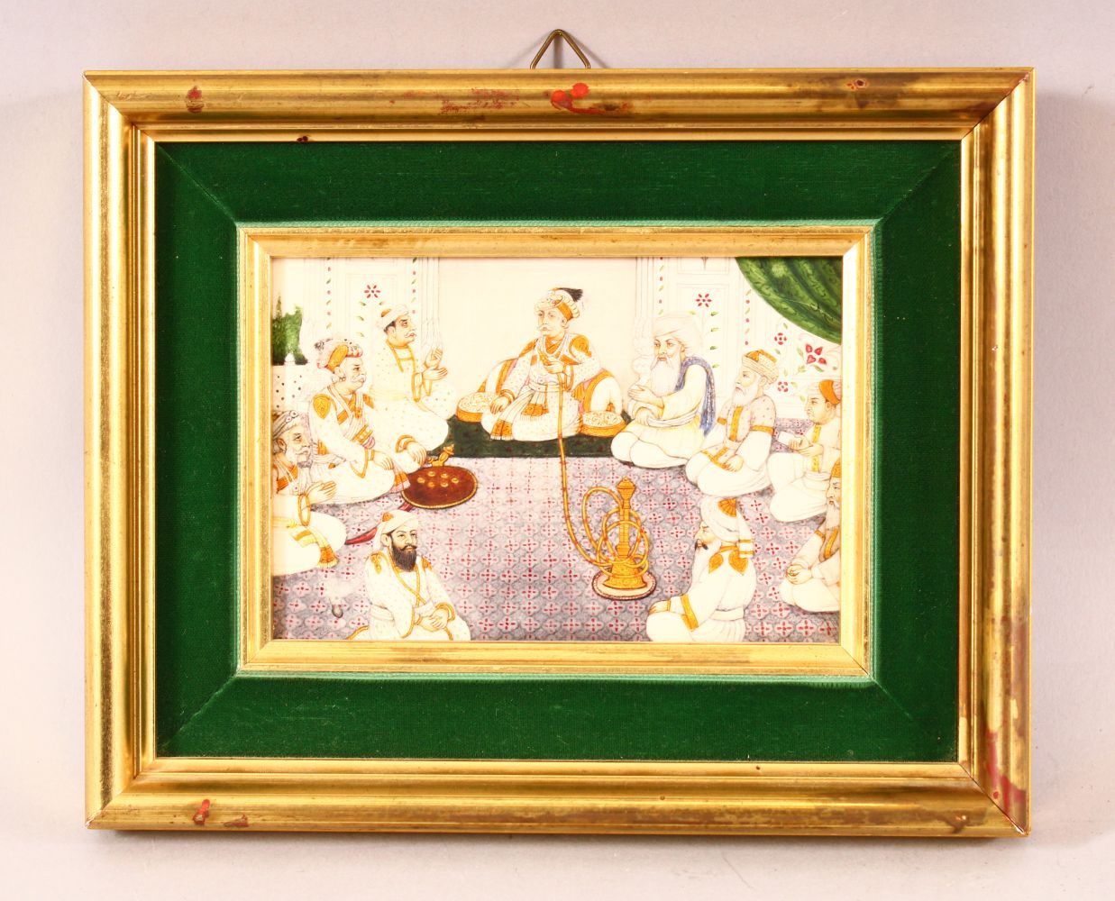 AN INDIAN MINIATURE PAINTING ON BONE OR IVORY - depicting male figures seated around a pipe - framed
