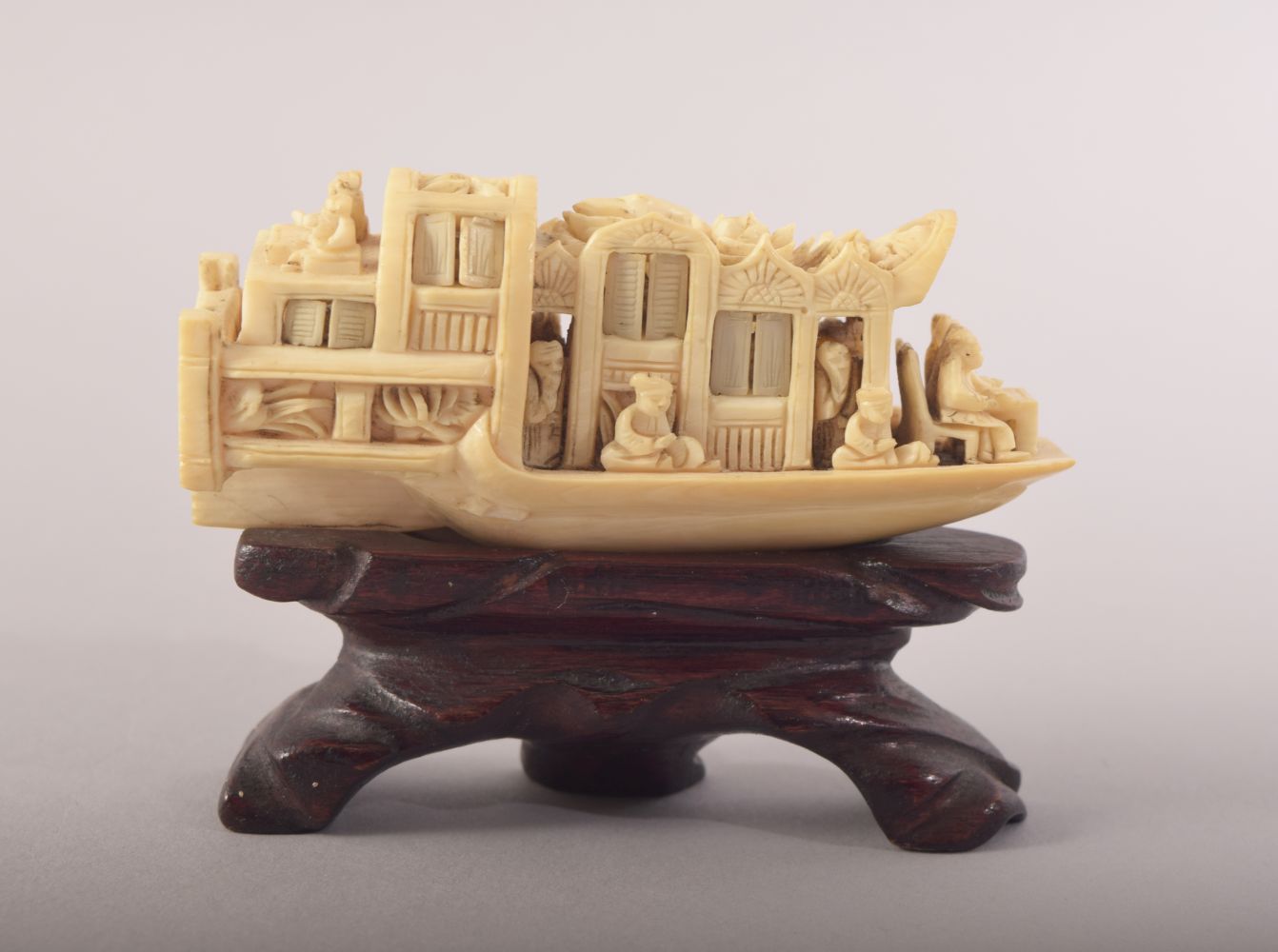 A SMALL CARVED IVORY MODEL OF A JUNK and wooden stand, 8cm long.