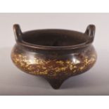 A CHINESE GILT SPLASH BRONZE TWIN HANDLE CENSER - on three feet with twin handles - the base with