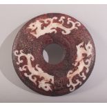 A SMALL CHINESE RED STAINED HARDSTONE BI DISK, with three stylised chilong, 10.5cm diameter.