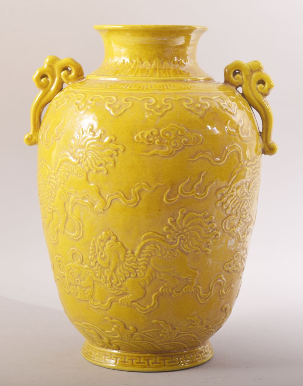 A CHINESE YELLOW GLAZED PORCELAIN TWIN HANDLE JAR - decorated in relief with two lion dogs amongst