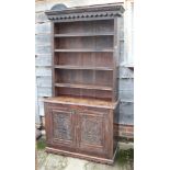 A carved oak dresser, the upper section fitted four shelves over cupboard enclosed two panelled