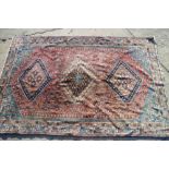 A Persian tribal rug with three hooked medallions to the centre red ground with all-over floral