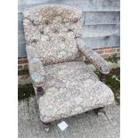 A button back low armchair, upholstered in a floral fabric, on turned and castored supports, an Arts