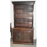 A carved oak dresser, the upper section fitted four shelves over cupboard enclosed two panelled