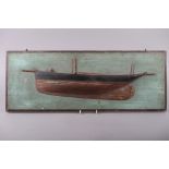 A carved and painted softwood scale model half hull of a yacht, on green painted backboard, 26" wide