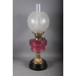 A cranberry glass oil lamp with etched shade, 23 1/2" overall, and a brass chamberstick and trivet