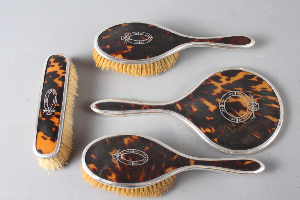 A silver pique and tortoiseshell dressing table set, comprising mirror, clothes brush and two hair