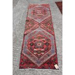 A Caucasian wool tribal runner with two diamond guls on a salmon ground, 77" x 26" approx