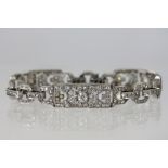 An Art Deco white metal and diamond bracelet comprising three rectangular panels with chain links,