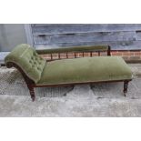An early 20th century polished as mahogany chaise longue with spindle back, upholstered in a green