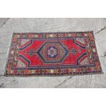 A wool tribal rug with central medallion and geometric border on a red ground, 67" x 35 1/2" approx