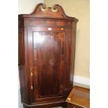 A George III crossbanded mahogany corner cupboard on stand with panel door enclosing shaped front