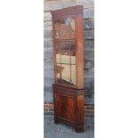 * A figured mahogany corner cabinet, the upper section enclosed lattice glazed door over one door,