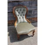 A late 19th century carved walnut showframe low seat nursing chair, upholstered in a green velour,