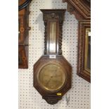 A dark oak cased octagonal barometer and thermometer, flanked by barley twist columns, 22 1/2" high