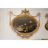 An oval gilt framed wall mirror with bevelled edge, swags, vase crest and ribbon decoration, plate