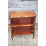 A mahogany three-tier book stand with spindle sides, on turned and castored supports, 26" wide x 16"