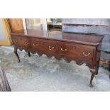 A Georgian dark oak sideboard with three long drawers over shaped carved scrolled frieze, on