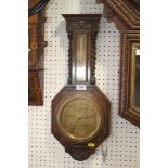 A dark oak cased octagonal barometer and thermometer, flanked by barley twist columns, 22 1/2" high,