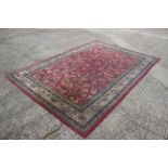 A Persian style machine woven rug with floral designs on a red ground in shades of natural, blue and