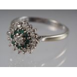 An 18ct white gold dress ring cluster set emeralds and diamonds, 4.4g gross, size R
