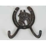 A double coat hook having horse head and horseshoe to centre, 12cm wide.